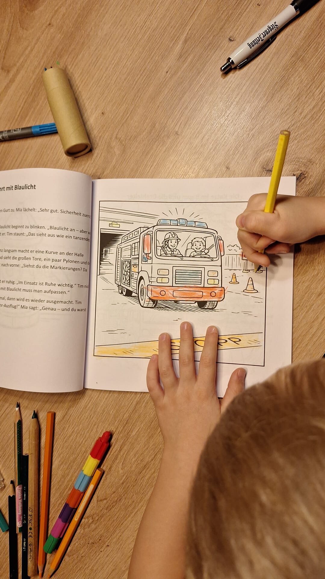 Ein Kind malt ein Feuerwehrfahrzeug im Brandschutz-Malbuch aus